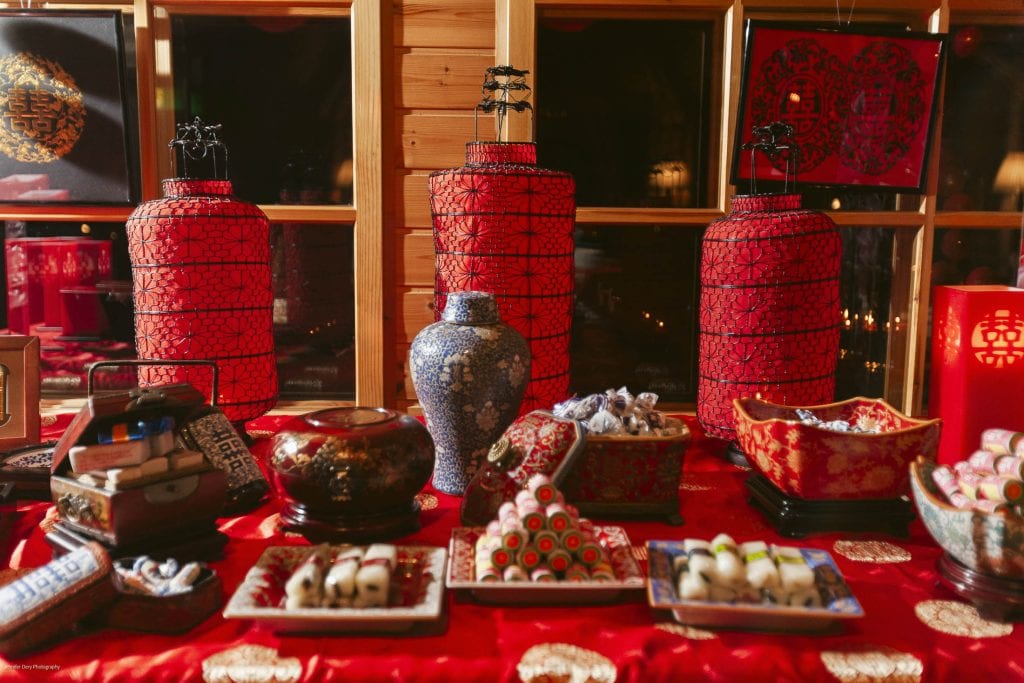 A festive table with traditional Chinese lanterns, vases, decorative boxes, and assorted sweets on a red cloth, celebrating a cultural event such as Lunar New Year.