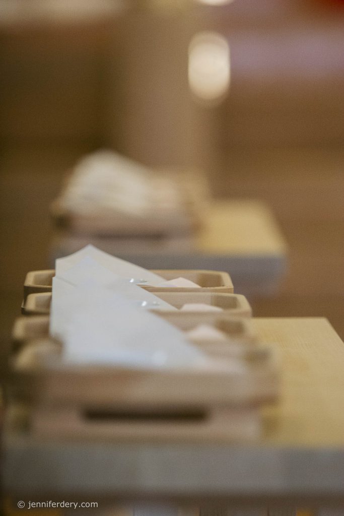 A close-up of neatly folded white napkins placed on wooden trays, arranged in a soft-focus, warm-toned setting.