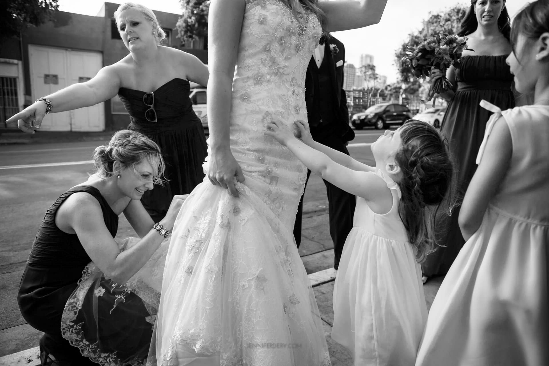 vision for wedding photos is documentary b&w wedding photos. here, a bride and flower girl. the little girl is trying to get the bride's attention while bridesmaids try to help in the background