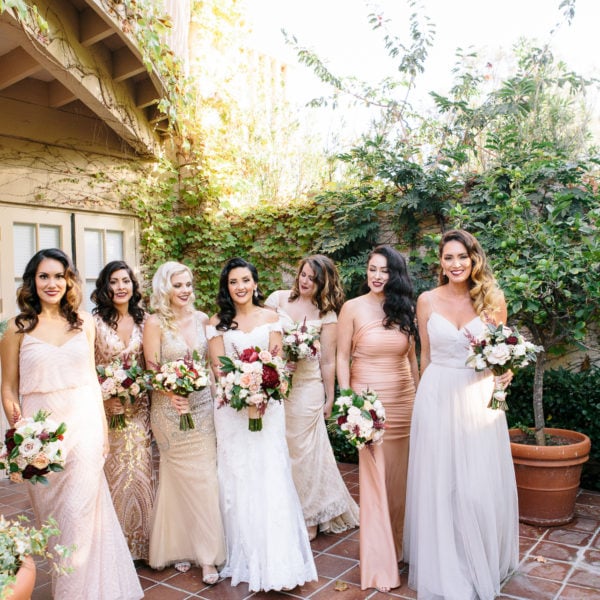 group of bridesmaids walking together on a terra cotta patio at rancho bernardo inn. women are all dressed in long dresses that are varying shades of light pink