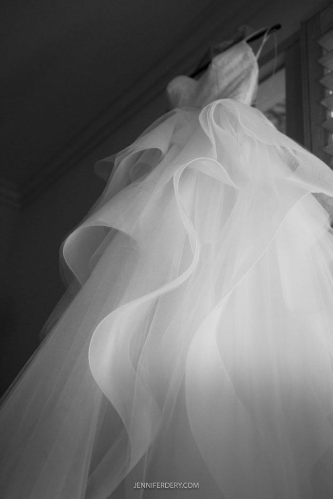 b&w image from below of a white wedding dress hanging in a dark room