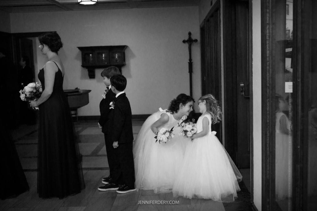 black and white documentary candid of flower girls in white long dresses playing before a wedding processional