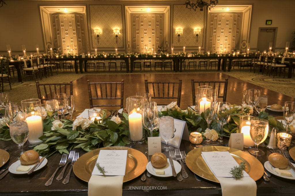 interior of the rancho bernardo inn ballroom decorated with gold, candles, and greenery along long tables for a wedding