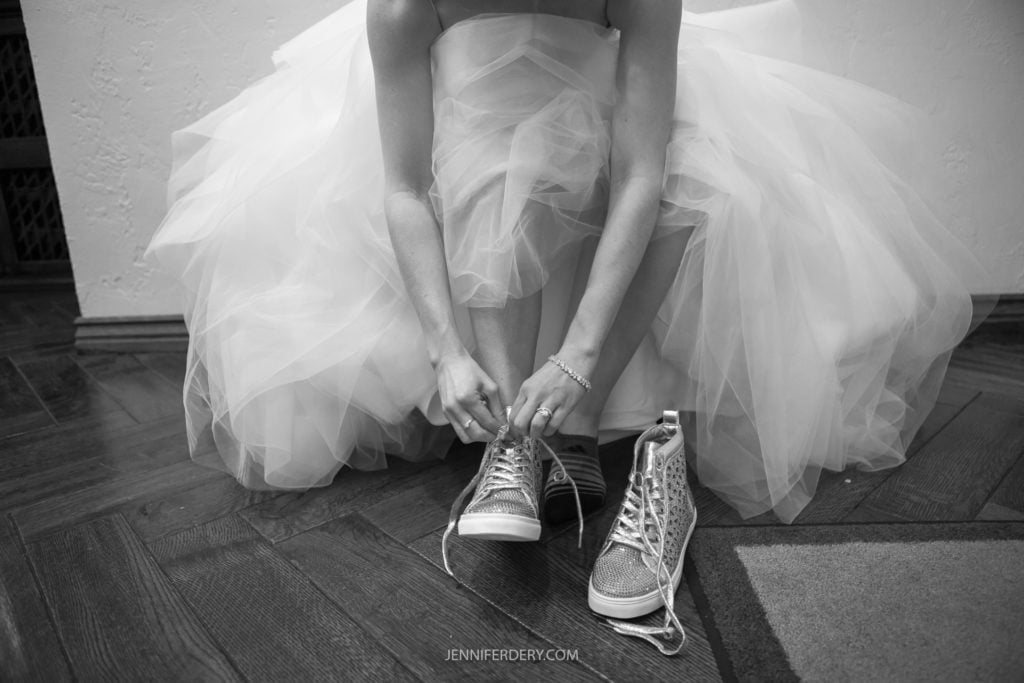 black and white candid image of bride putting on her sneakers to go dance at her wedding