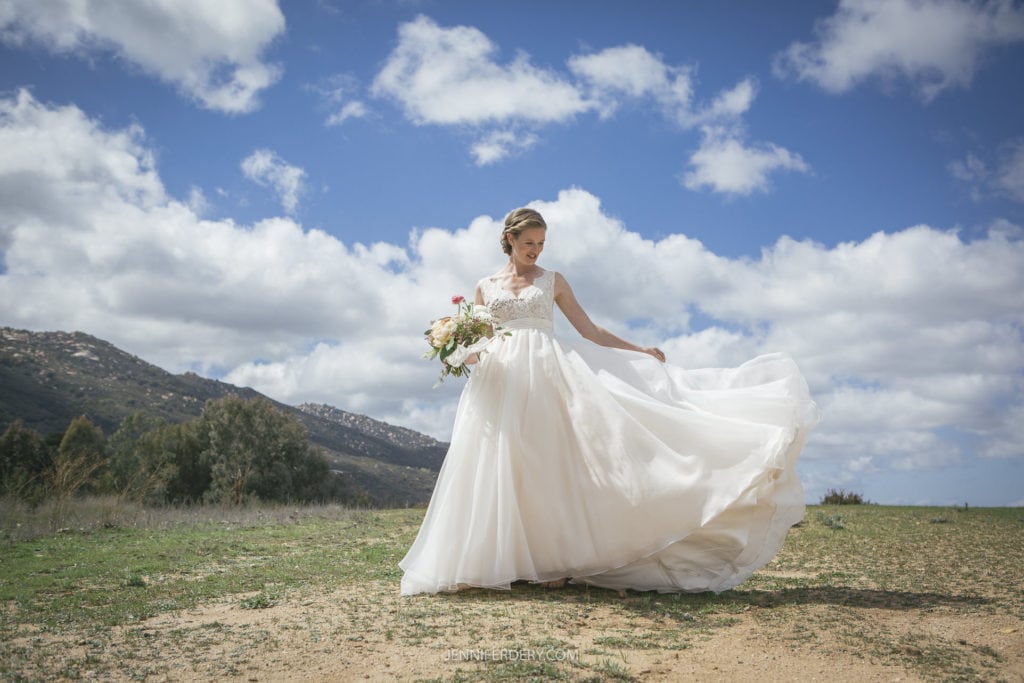 bride in the mountain field in full sun with fluffy clouds and a long white dress