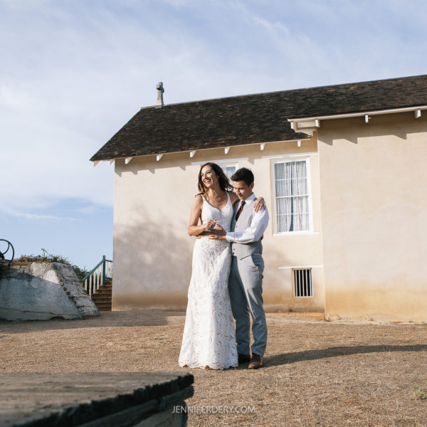 wedding couple shown embracing standing adjacent to the wedding ceremony lawn at Rancho Guajome Adobe in vista
