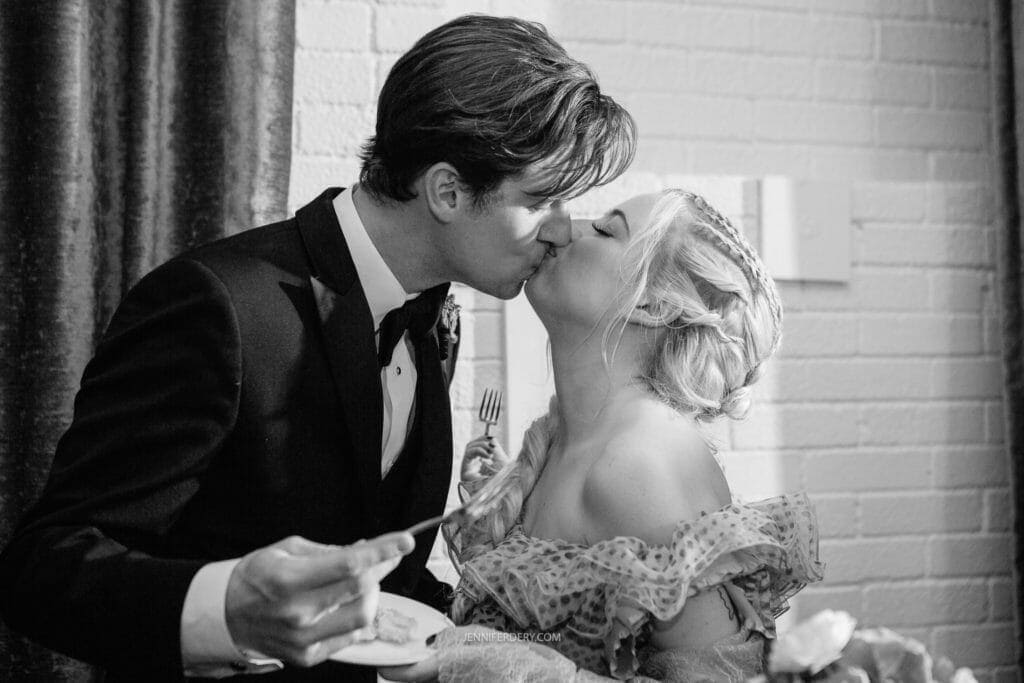 balck and white photo of a couple kissing after cutting their wedding cake