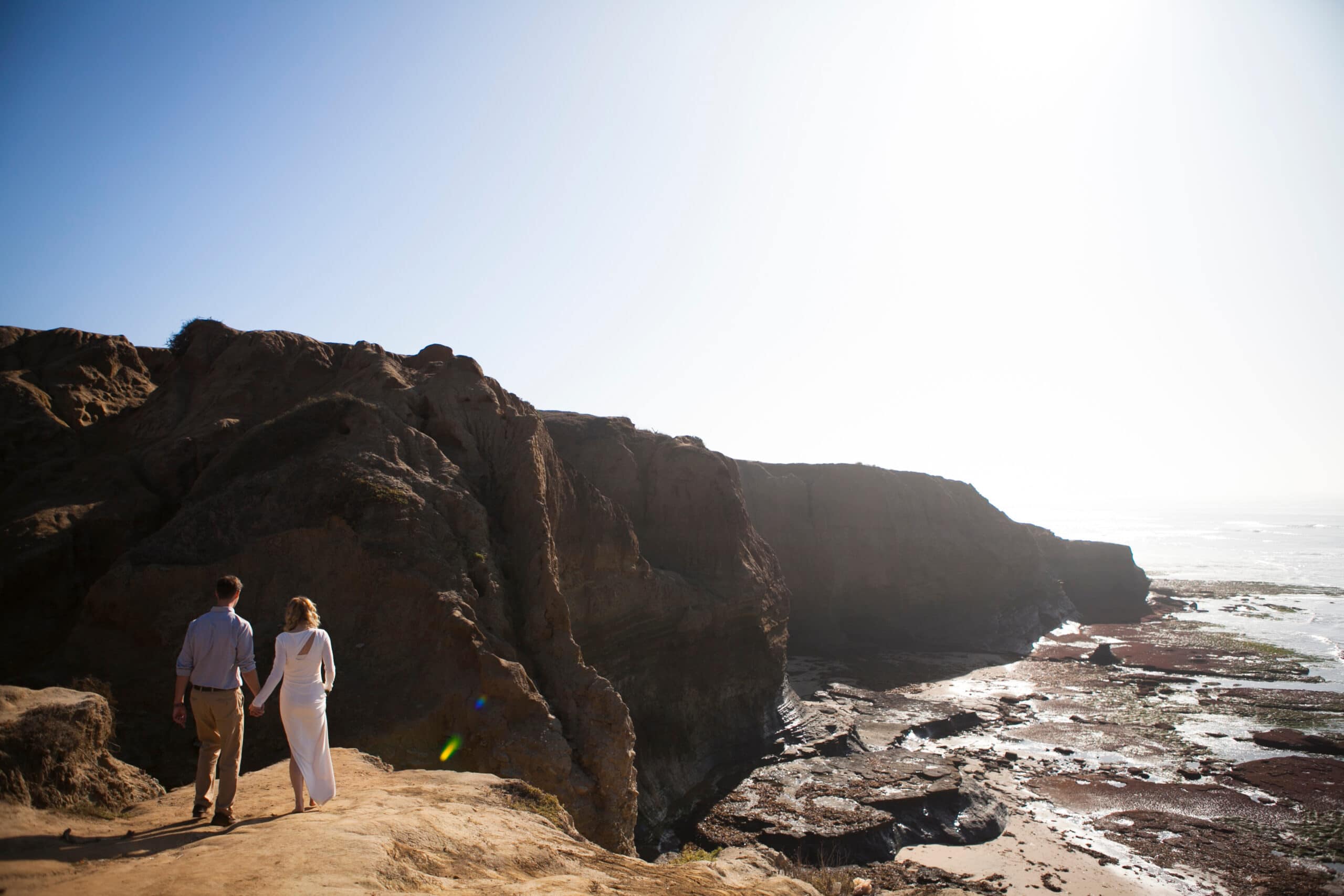 sunset cliffs elopement wedding and portrait of a couple walking along the cliff at late afternoon. photographer is positioned higher-up on the cliff to get a broad view of the ocean.
