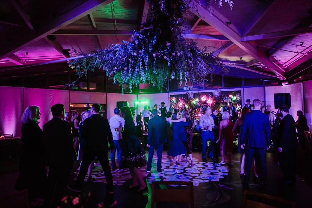 photo of the dance floor full of people lit by purple and green lights during a reception at the university club in palo alto, ca