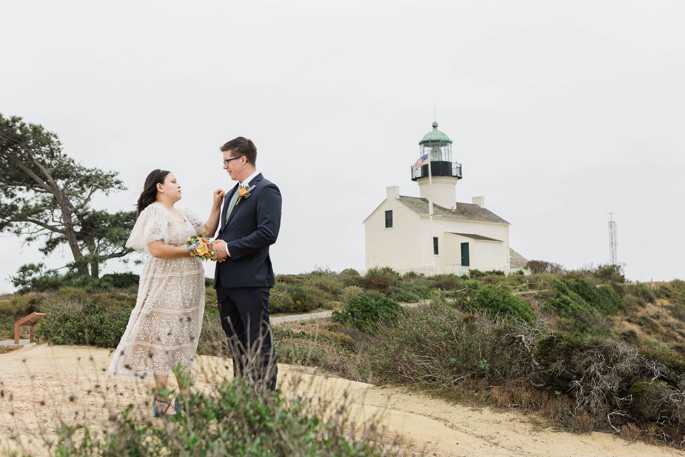 elopement photo of a bride and groom standing cliffside in san diego shown with cabrillo monument lighthouse in the background