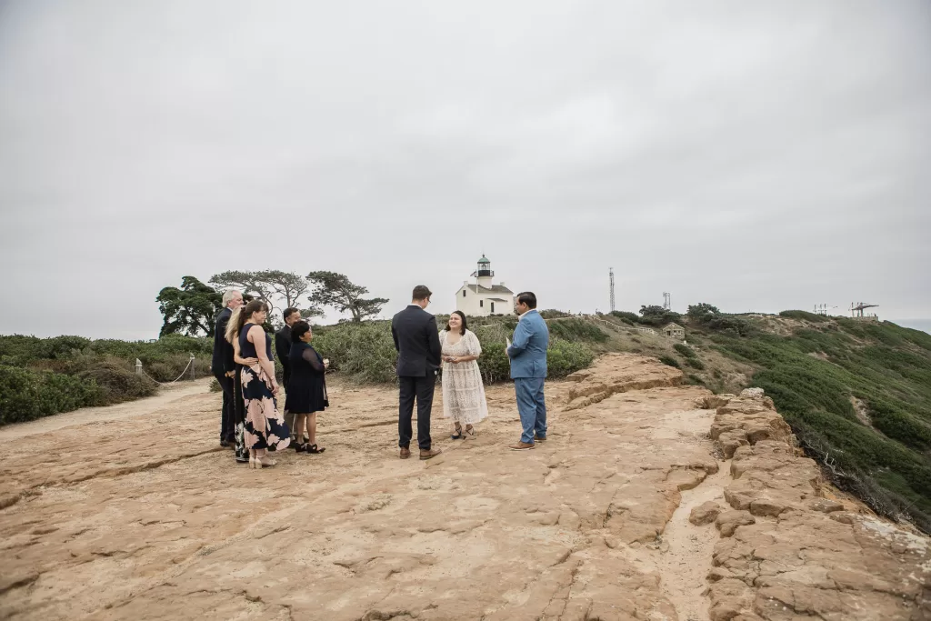 elopement ceremony photo of a bride and groom and a few family members standing cliffside in san diego at cabrillo monument park with the ocean in the background