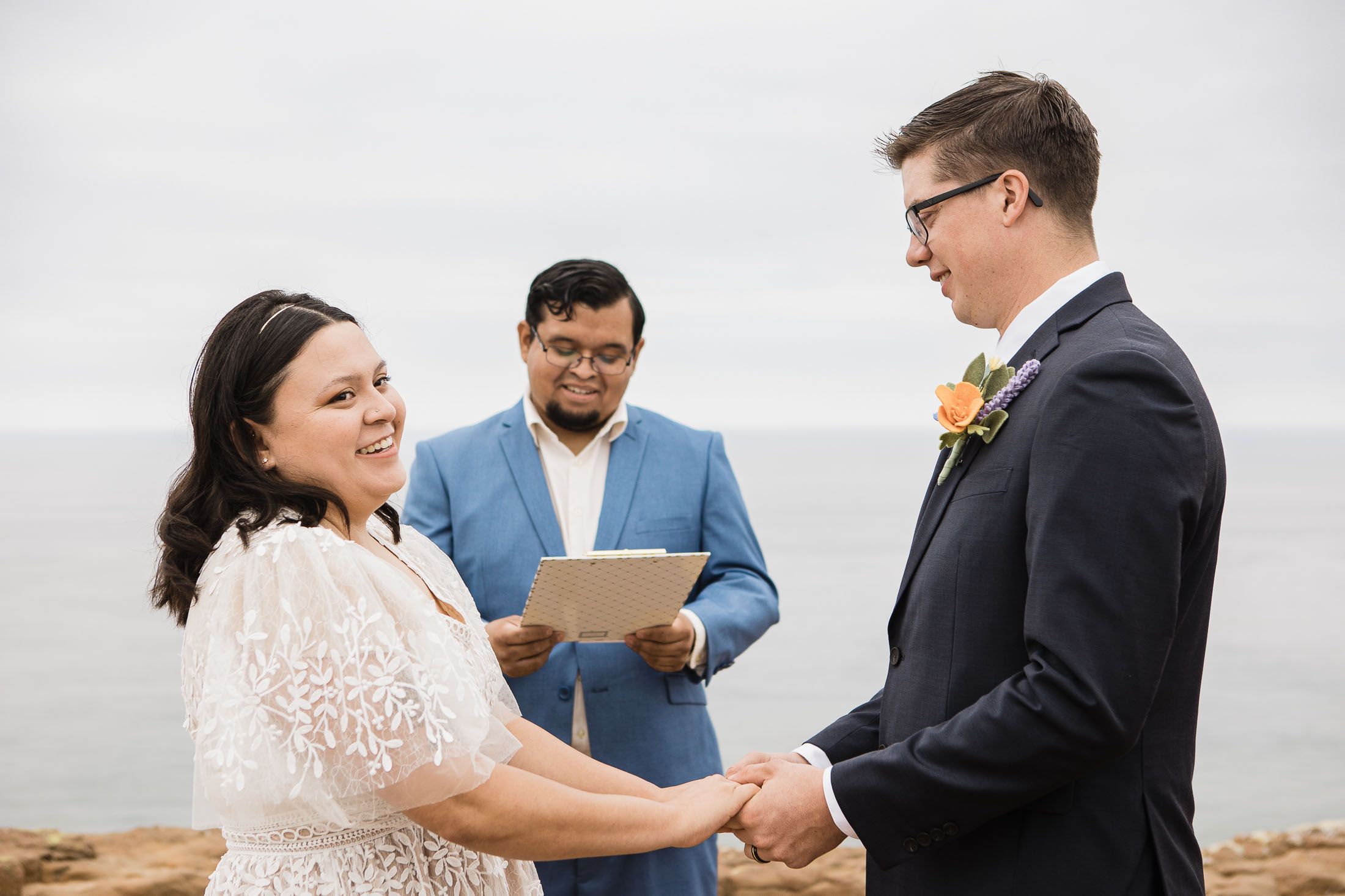 elopement ceremony photo of a bride and groom standing cliffside in san diego at cabrillo monument park with the ocean in the background
