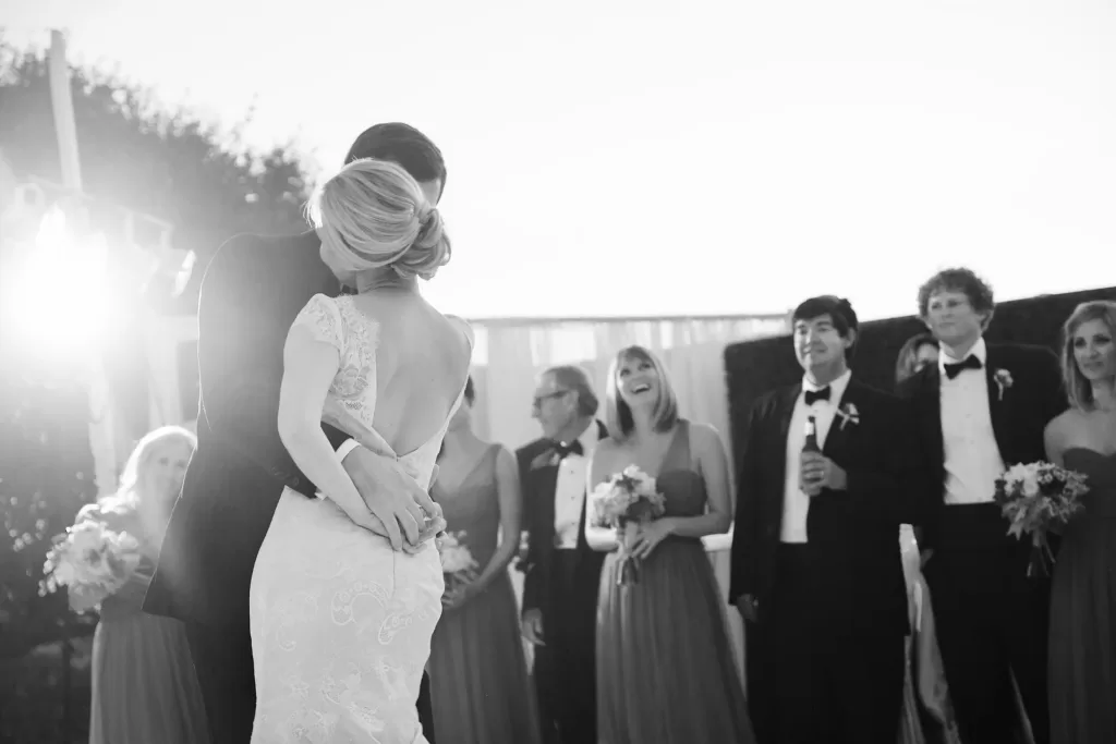 black and white photo of a wedding couple during their first dance with bridal party in the background. shown on croquet lawn at rancho valencia hotel