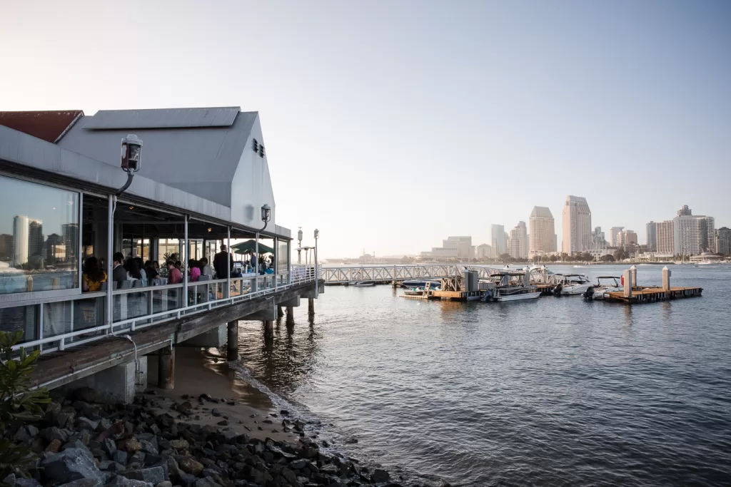 color photos of a destination wedding rehearsal location at peohe's restaurant coronado. skyline and boat dock in background, water in foreground