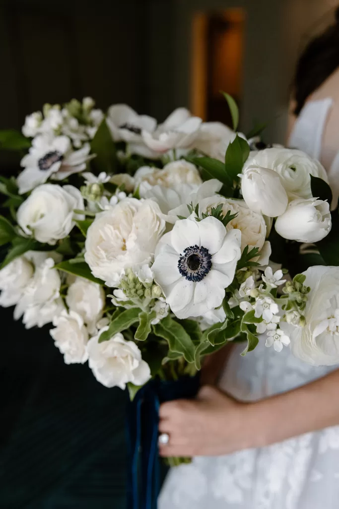 white wedding bouquet featuring anemones, stock, roses, and ranunculus. wrapped in navy velvet ribbon