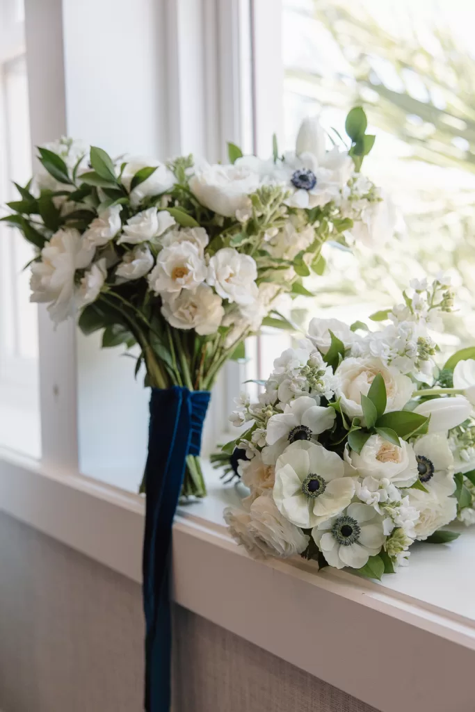 white wedding bouquet featuring anemones, stock, roses, and ranunculus. wrapped in navy velvet ribbon