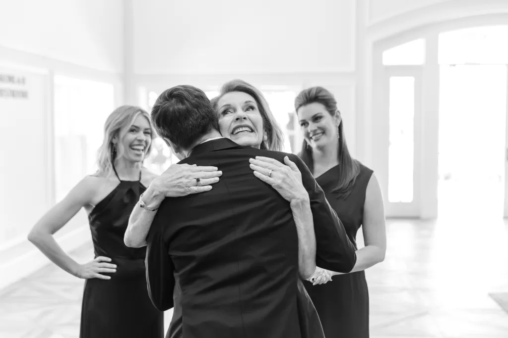 B&W photo of a groom hugging his mom with his sisters in the background