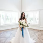 full-length photo of a bride in a white lace dress and white wedding bouquet with navy ribbon