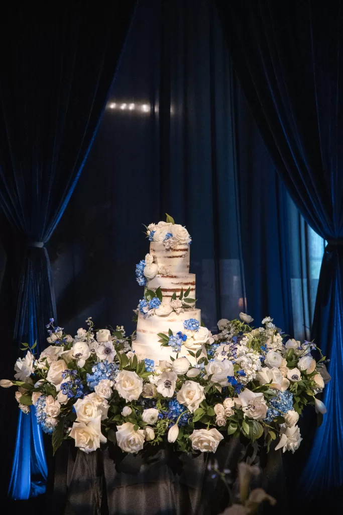 white floral arrangements, rough-frosted wedding cake, candles, and navy draped ballroom of southpointe ballroom at the hotel del coronado, CA