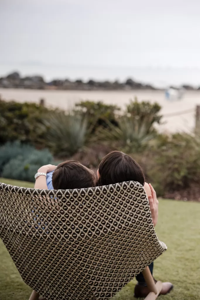 destination engagement session at the hotel del coronado in san diego, california. photo of a couple snuggling in a chair with ocean in the background