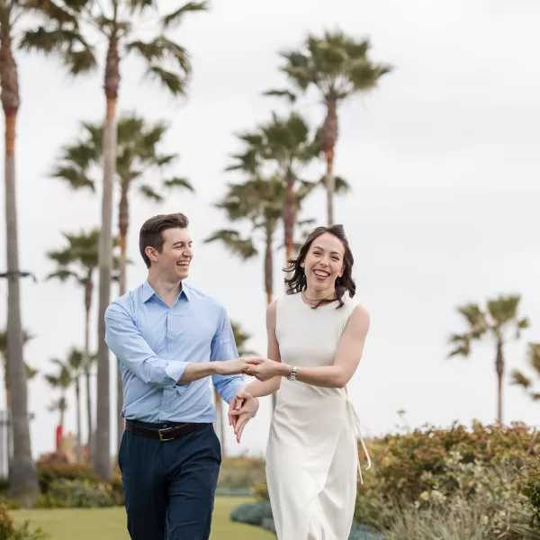 couple holding hands on lawn at the hotel del coronado in san diego. white dress and blue button-down with navy pants