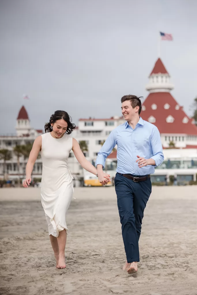 destination engagement session at the hotel del coronado in san diego, california. photo of a couple running holding hands with the hotel in the background